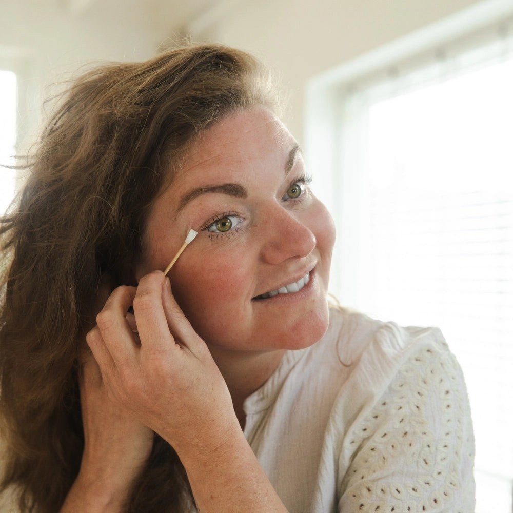 Eine Frau nutzt das wiederverwendbare Silikon-Wattestäbchen von Bamboovement zur präzisen Korrektur ihres Make-ups am Auge vor einem hellen Badezimmerspiegel.