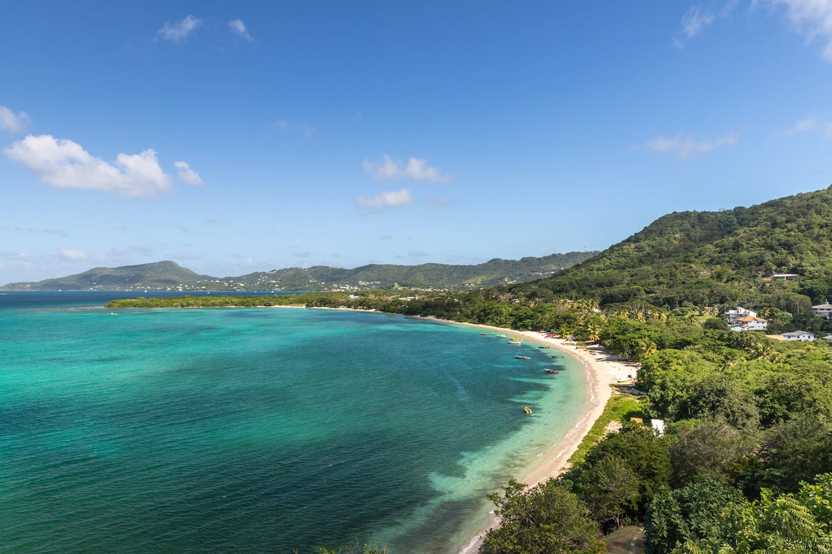 Panorama einer geschwungenen, bewaldeten Bucht mit hellem Sandstrand und schimmerndem, türkisfarbenem Wasser.