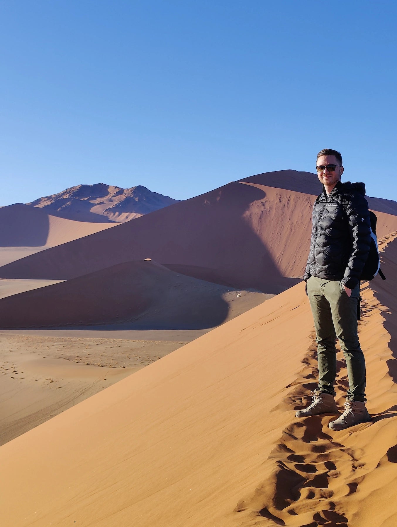 Pascal, der Gründer von trekaro, steht auf einer Düne in Namibia und lächelt in die Kamera.