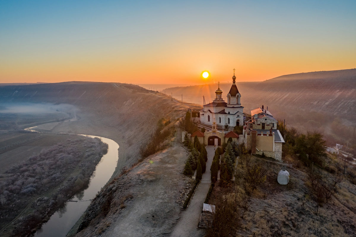 Luftaufnahme einer orthodoxen Kirche auf einem schmalen Bergkamm über einer Flussschleife bei Sonnenaufgang mit leichtem Nebel im Tal.