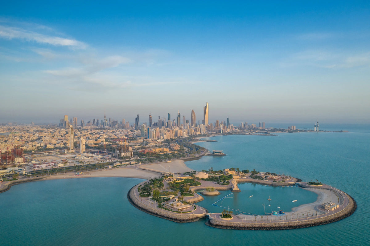 Luftaufnahme der künstlichen Halbinsel Green Island im türkisfarbenen Persischen Golf mit der modernen Skyline von Kuwait-Stadt im Hintergrund.