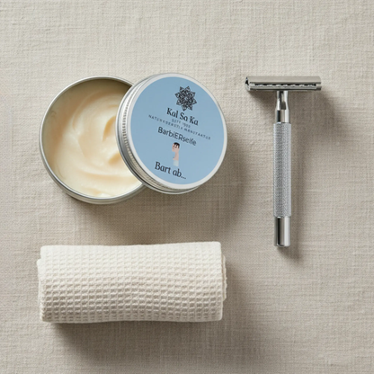Draufsicht auf ein Rasur-Set: eine offene Dose Kal Sa Ka Barbierseife, ein silberner Rasierhobel und ein gerolltes, beiges Waffeltuch auf einem Leinenhintergrund.