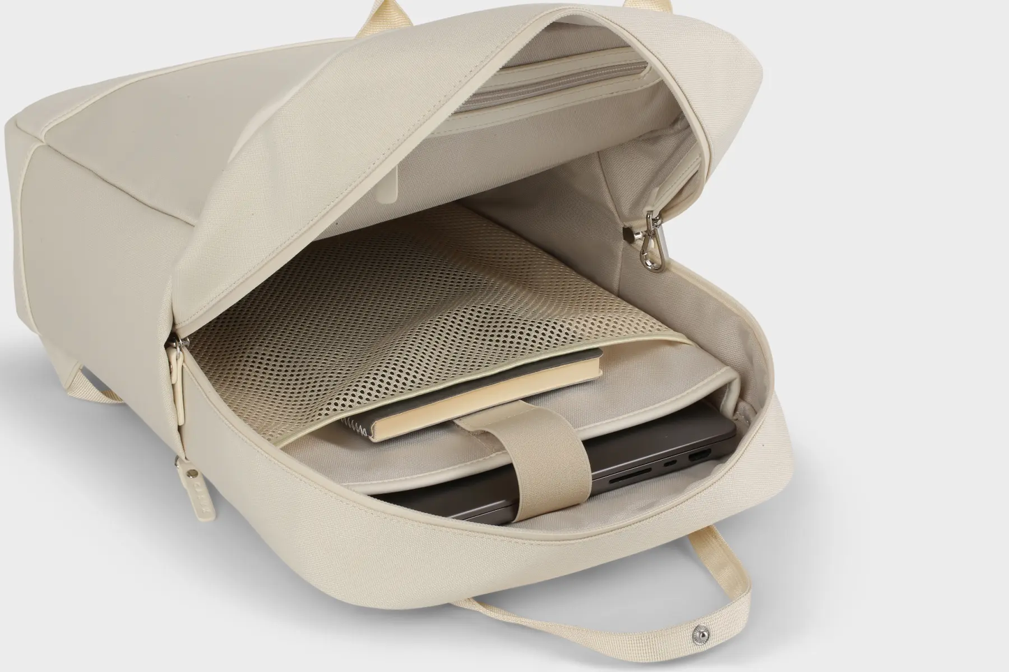Geöffneter, beigefarbener Rucksack der Marke Casyx, der das Hauptfach mit einem Laptop im gepolsterten Fach, einem Notizbuch und einer inneren Netztasche zeigt.