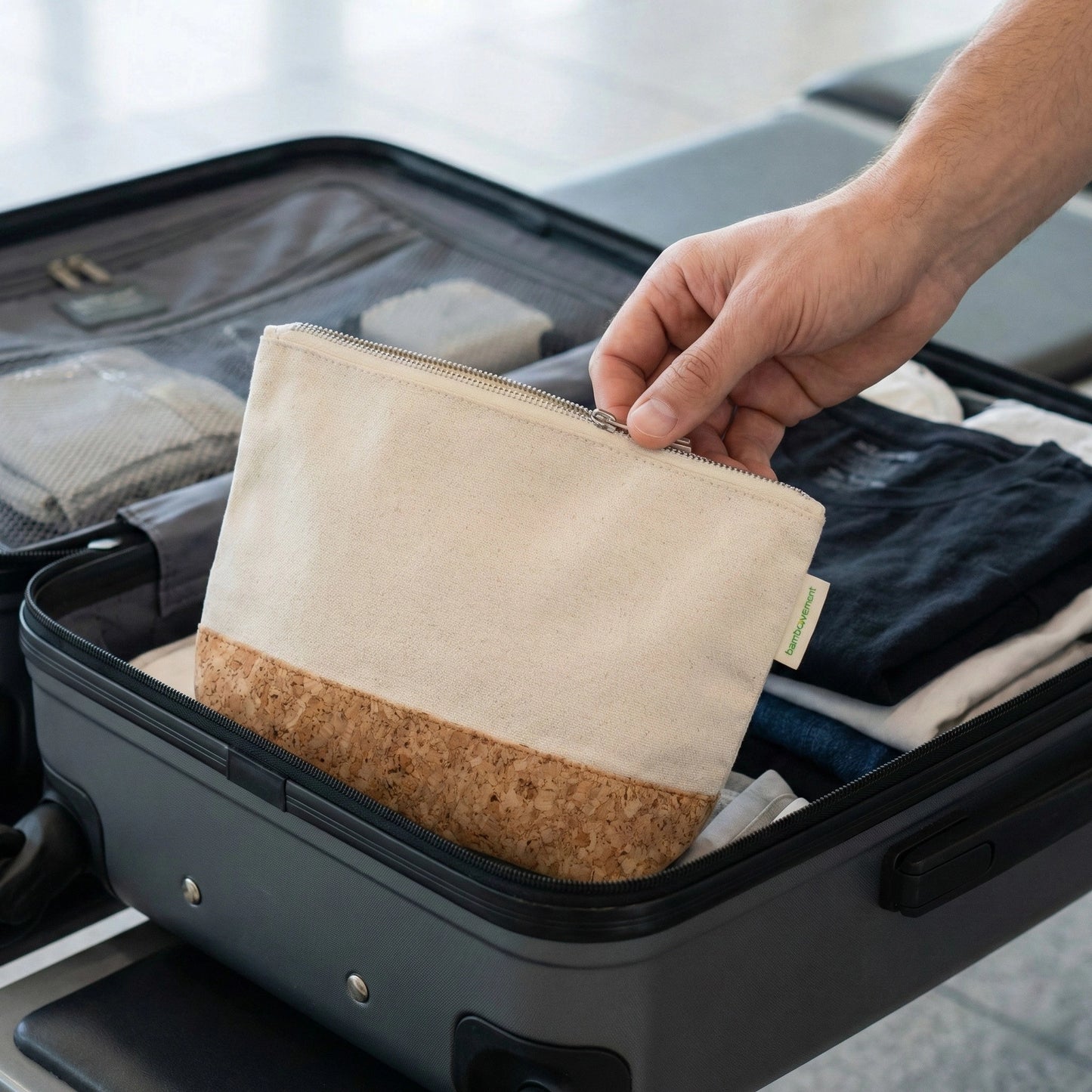 Nachhaltig reisen: Eine Hand legt den plastikfreien Kulturbeutel aus Kork und Baumwolle von Bamboovement in einen gepackten Koffer.