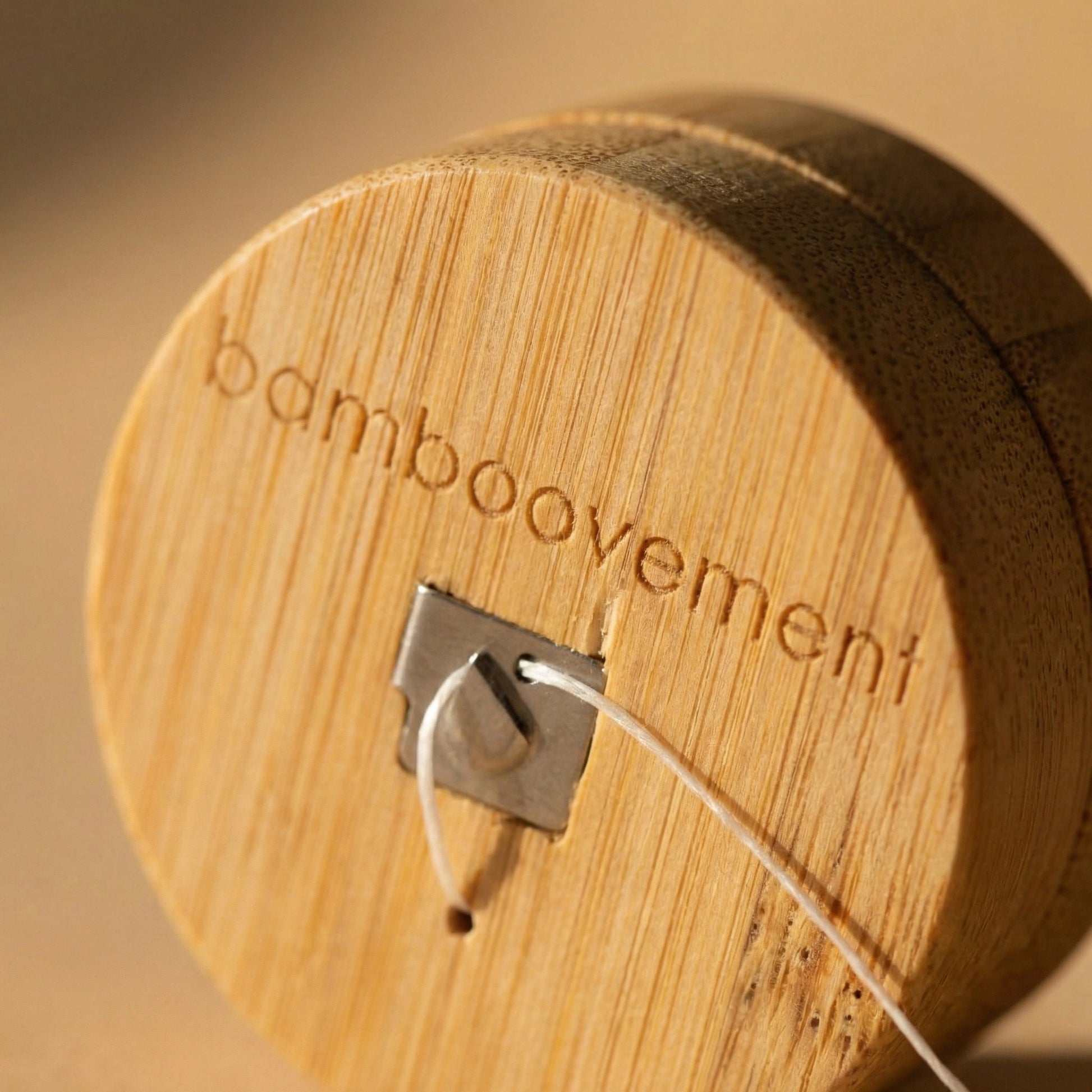 Nahaufnahme des runden Bambusbehälters für die umweltfreundliche Zahnseide von Bamboovement mit graviertem Markenlogo und integriertem Metall-Abriss.