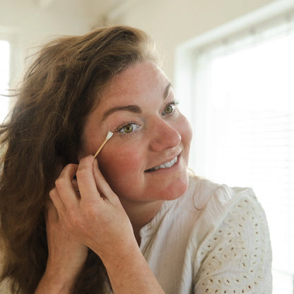 Eine Frau nutzt das wiederverwendbare Silikon-Wattestäbchen von Bamboovement zur präzisen Korrektur ihres Make-ups am Auge vor einem hellen Badezimmerspiegel.