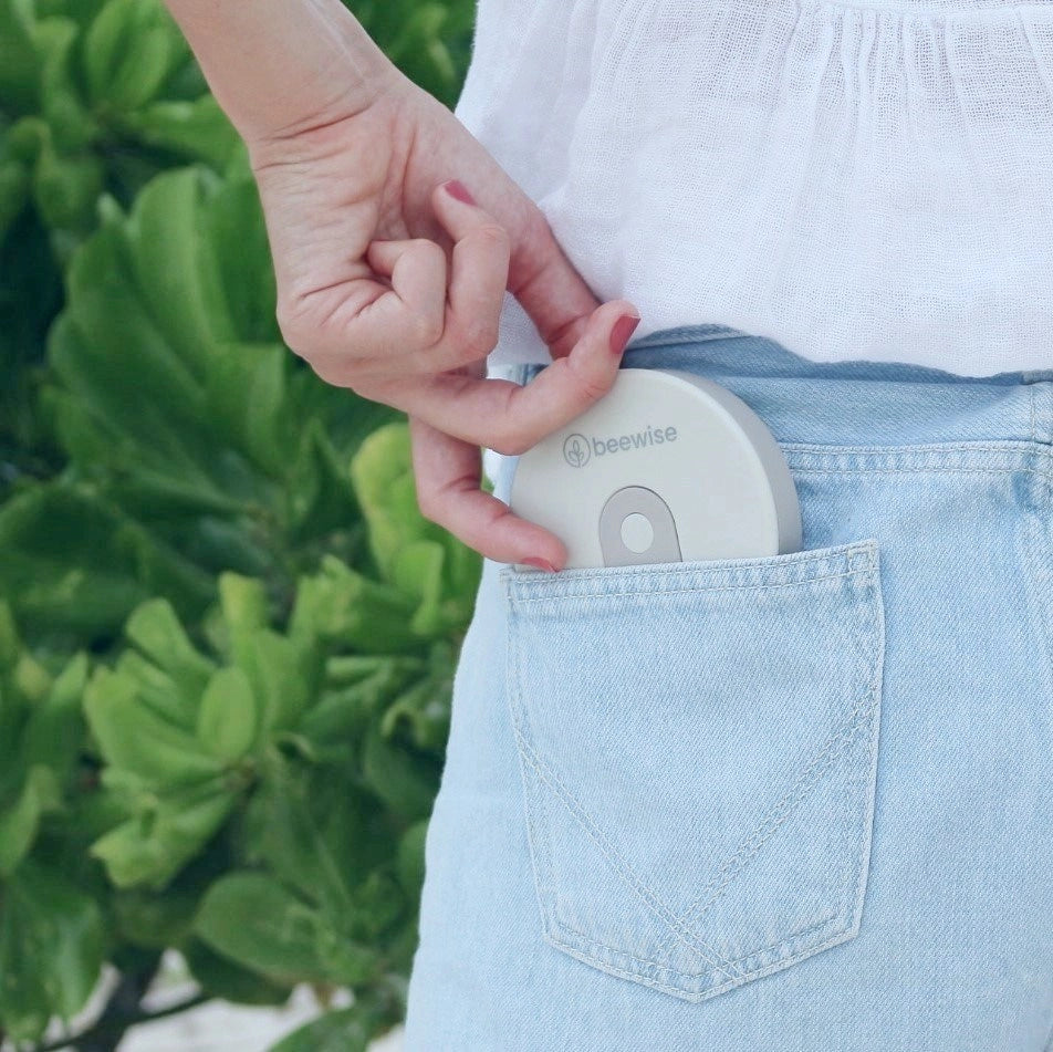 Eine Hand schiebt die flach zusammengefaltete, graue beewise Kaffeetasse in die Gesäßtasche einer hellblauen Jeans – platzsparender Begleiter für unterwegs.
