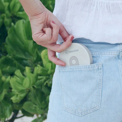 Eine Hand schiebt die flach zusammengefaltete, graue beewise Kaffeetasse in die Gesäßtasche einer hellblauen Jeans – platzsparender Begleiter für unterwegs.