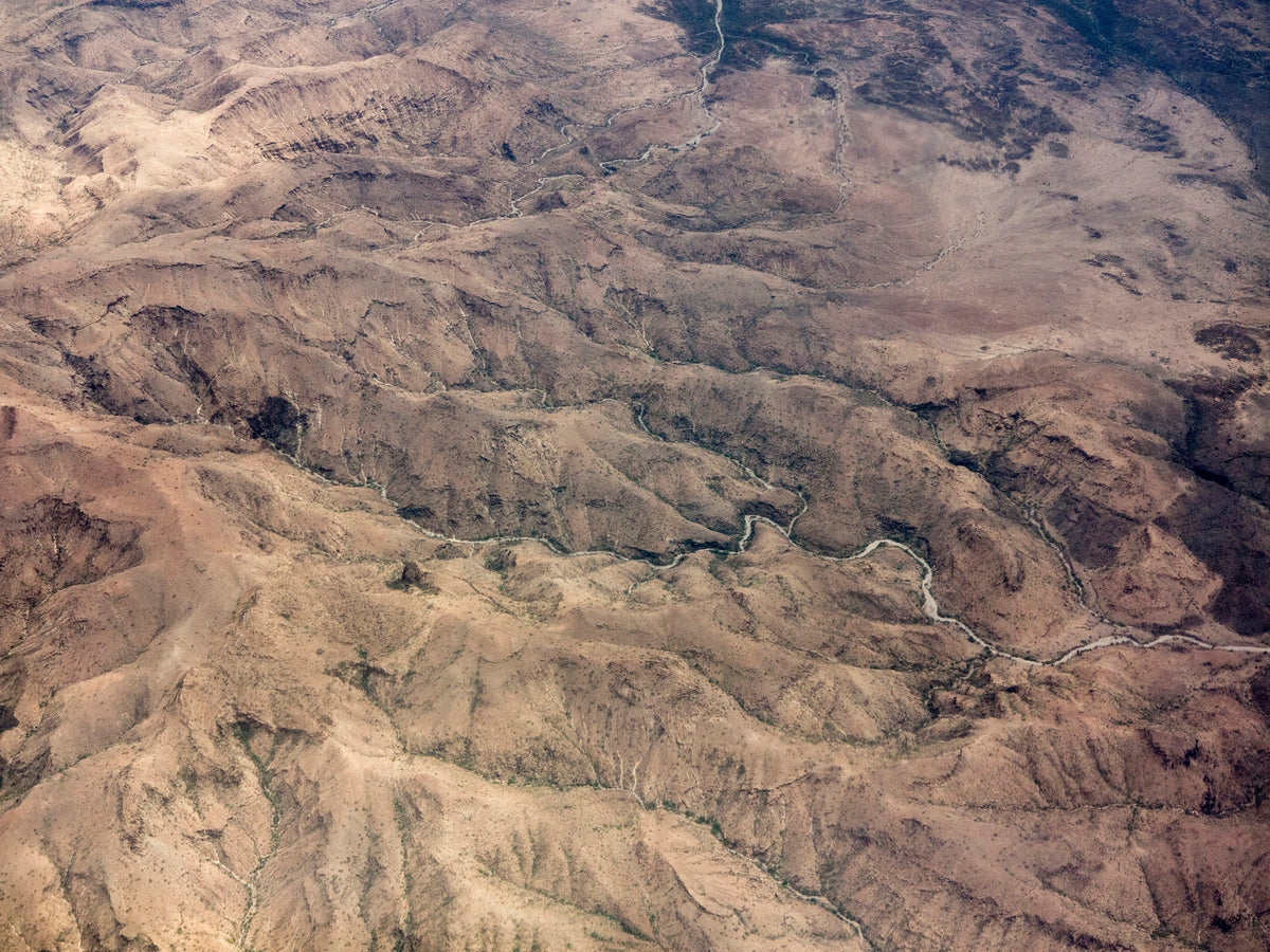 Luftaufnahme einer kargen, erdfarbenen Gebirgslandschaft in Somalia mit ausgetrockneten Flussbetten und felsigen Hügeln.