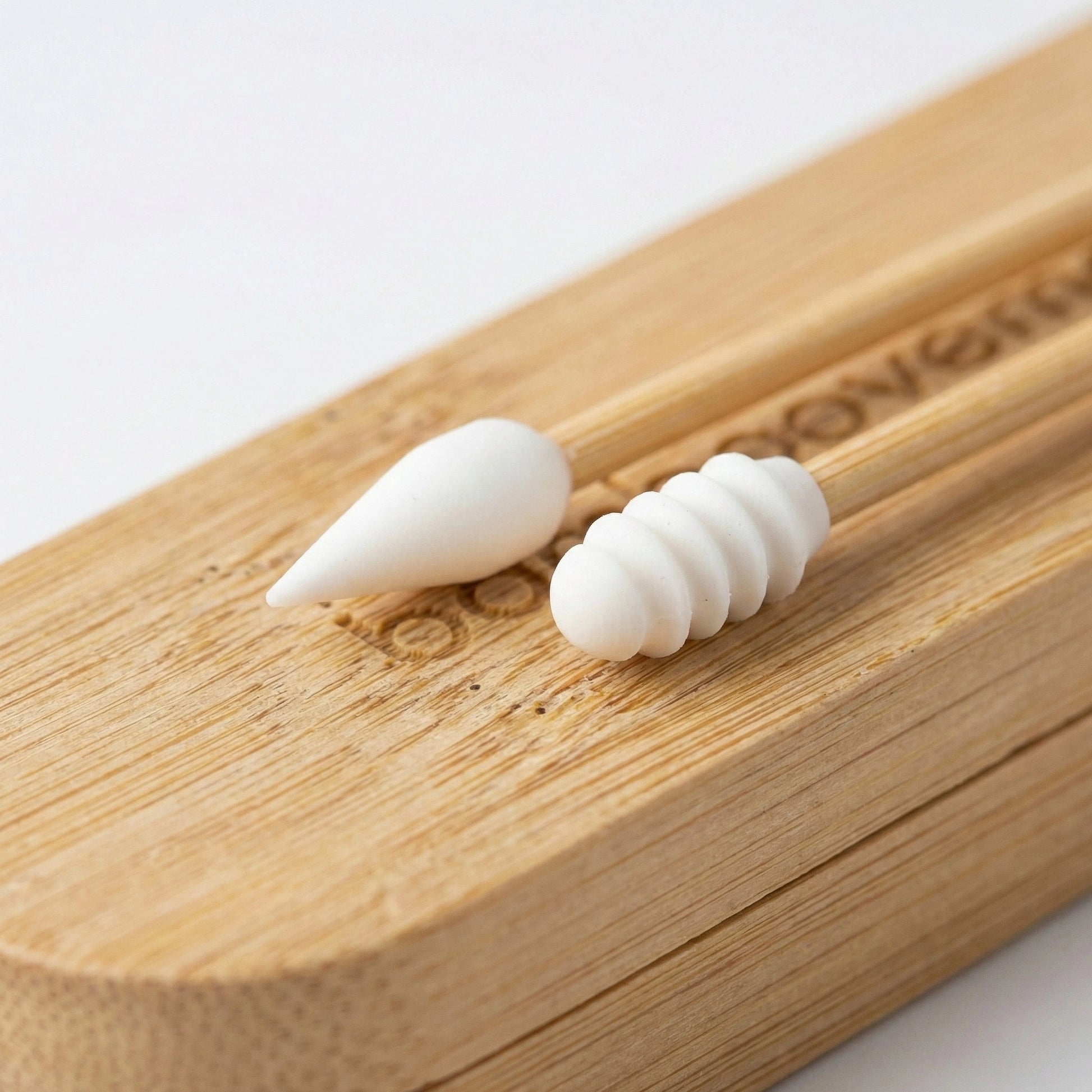 Draufsicht auf zwei verschiedene wiederverwendbare Wattestäbchen aus Silikon mit Bambusschaft, die auf ihrem passenden, gravierten Bambusetui liegen.
