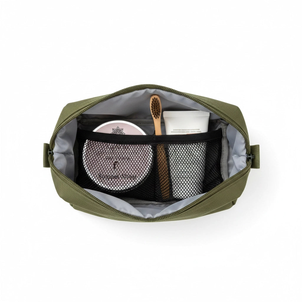 Blick von oben in eine grüne Kulturtasche mit der 'Stoppel Stopp' Reiserasierseife, einer Bambuszahnbürste und einer Tube Naturkosmetik – ideal für das Handgepäck.