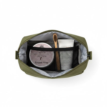 Blick von oben in eine grüne Kulturtasche mit der 'Stoppel Stopp' Reiserasierseife, einer Bambuszahnbürste und einer Tube Naturkosmetik – ideal für das Handgepäck.