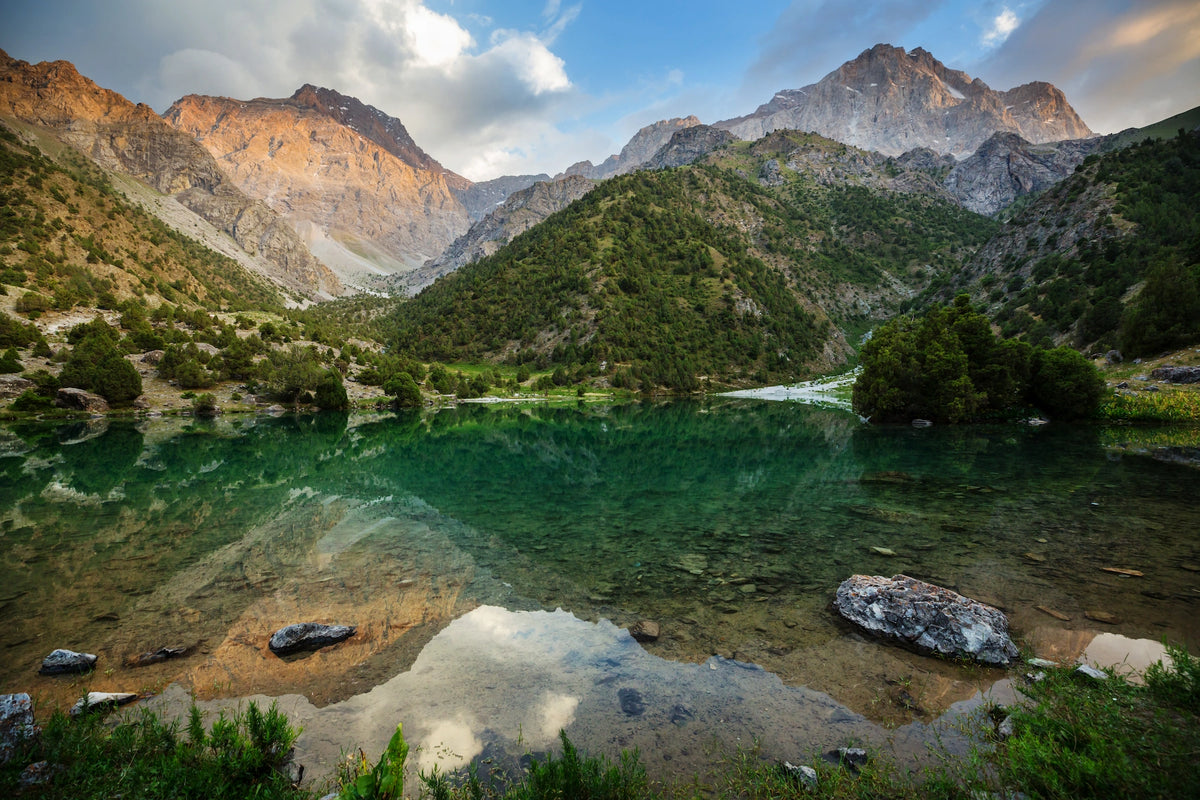 Kristallklarer, grünlich schimmernder Bergsee, in dem sich die umliegenden felsigen Gipfel und Hänge des Fan-Gebirges spiegeln.