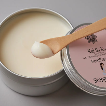 Nahaufnahme der cremigen weißen Textur der veganen Rasierseife 'Stoppel Stopp', die mit einem Holzspatel aus der Dose entnommen wird.